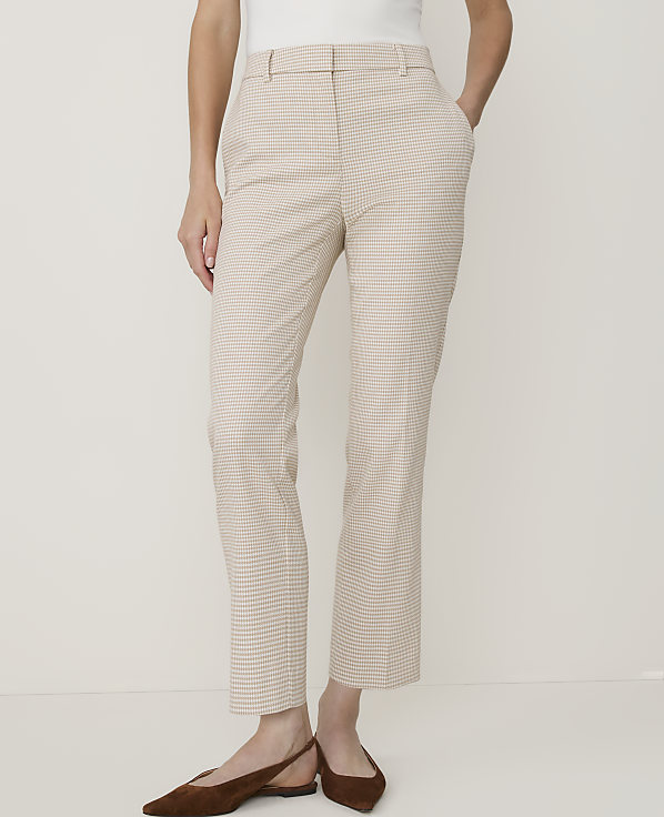 A person stands in a plain, light-colored room wearing beige and white checkered pants and brown flats.