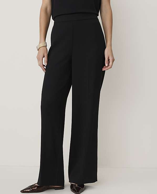 A person wearing black wide-leg pants and patterned flats stands against a plain white background.