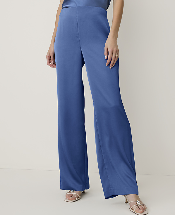 A person wearing blue wide-leg pants and strappy sandals stands against a plain, light-colored background.