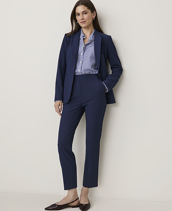 A woman in a navy blue suit and striped shirt stands against a plain white background.