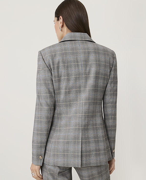 A woman in a grey plaid blazer and pants stands against a plain white background.