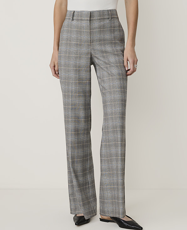 A person stands in the foreground wearing plaid trousers and black flats against a plain, light-colored background.