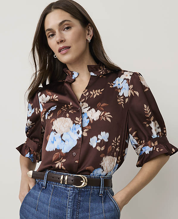 A woman in a floral brown blouse and blue jeans stands against a plain white background.
