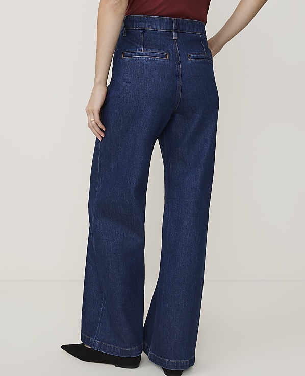 A person wearing dark wash wide-leg jeans stands against a plain white background.