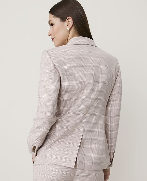 A woman in a light-colored plaid blazer and matching pants stands against a plain, light background.