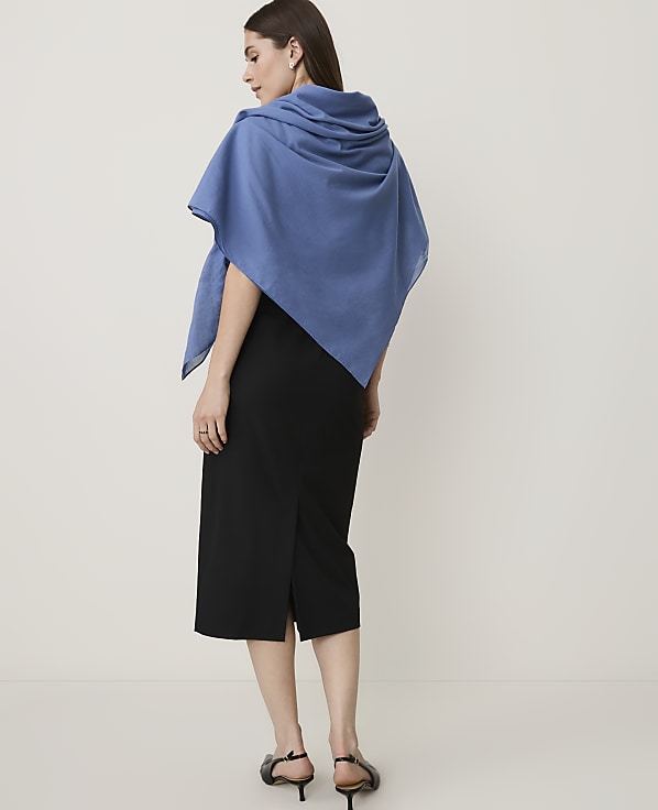 A woman in a black skirt and blue shawl stands against a plain white background.