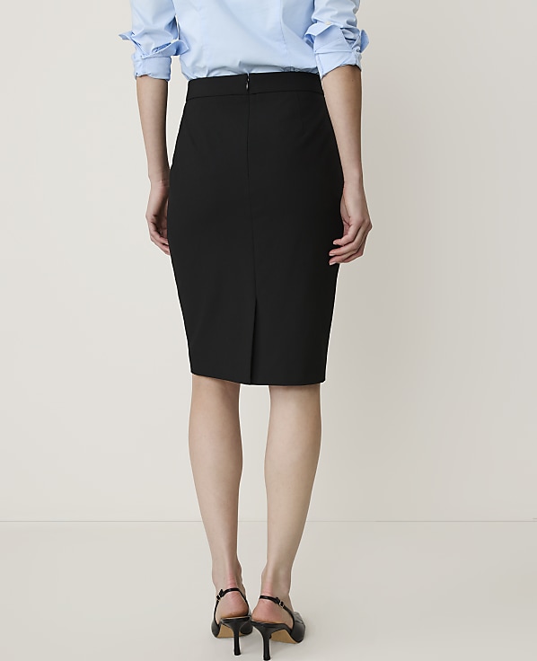 A woman in a light blue shirt and black pencil skirt stands against a plain white background.