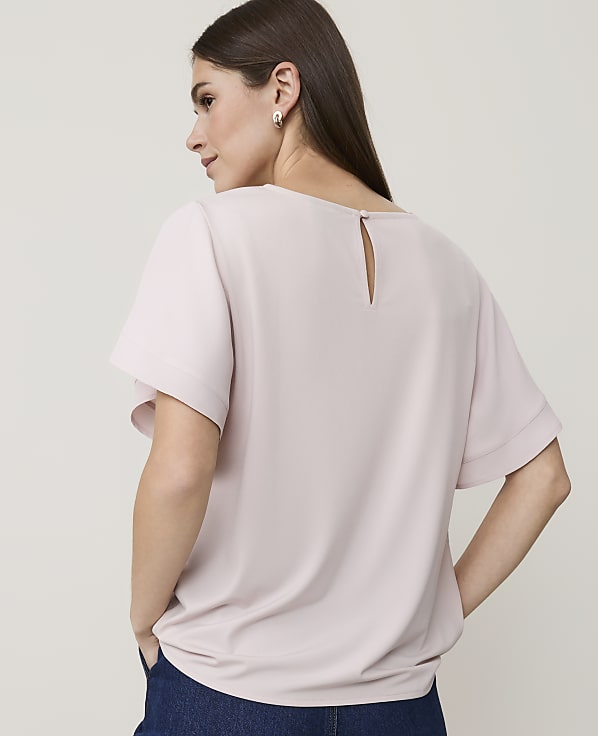 A woman in a pale pink top stands with her back to the viewer against a plain, light background.
