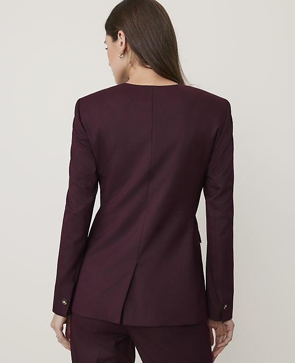 A woman in a burgundy blazer and pants stands against a plain white background.