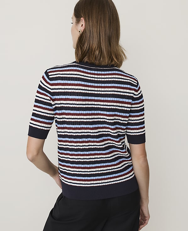 A woman in a striped sweater stands against a plain white background.