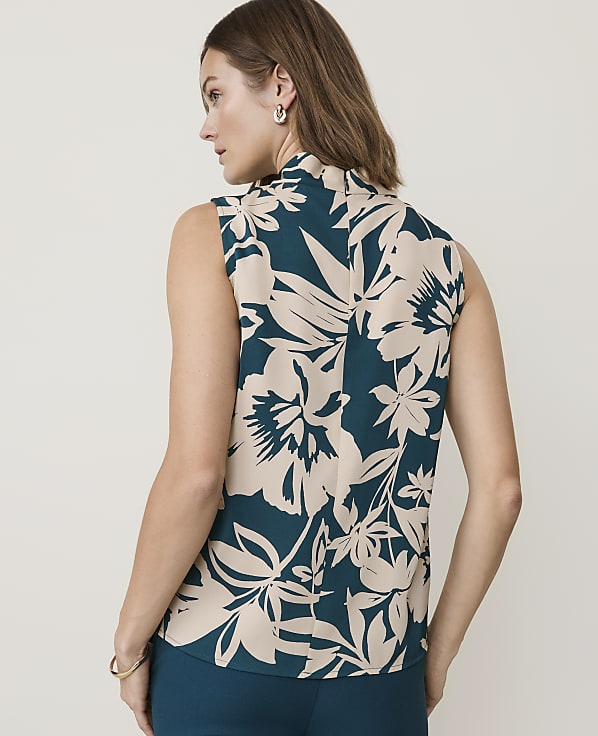 A woman in a sleeveless floral top stands against a plain, light-colored background.