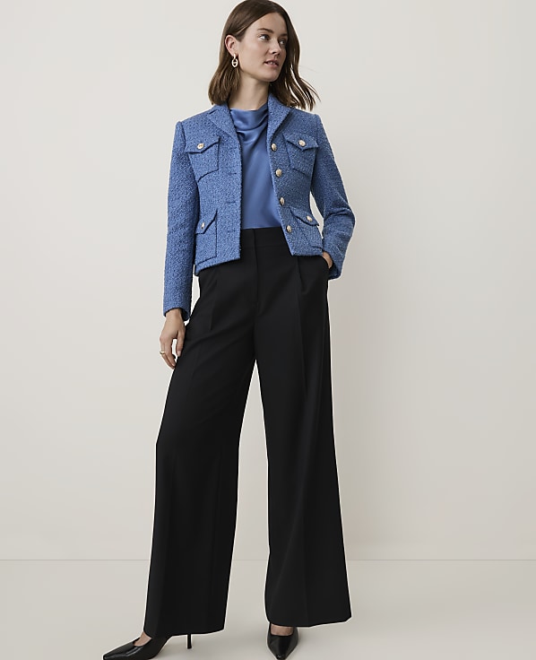 A woman in a blue tweed jacket and black wide-leg pants stands against a plain, light-colored background.