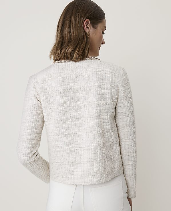 A woman in a cream tweed jacket stands against a plain, light background.