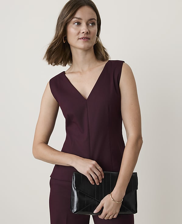 A woman in a burgundy V-neck top and pants holds a black clutch against a plain, light background.