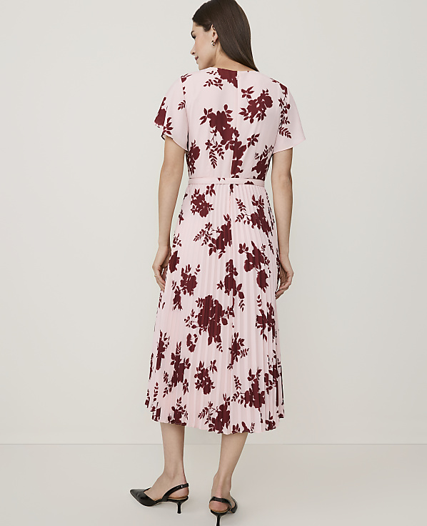A woman in a pink floral dress stands against a plain, light-colored background.