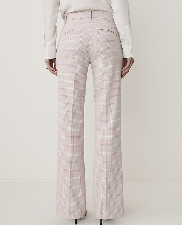 A person stands in front of a plain background wearing high-waisted, wide-leg plaid trousers and a white blouse.