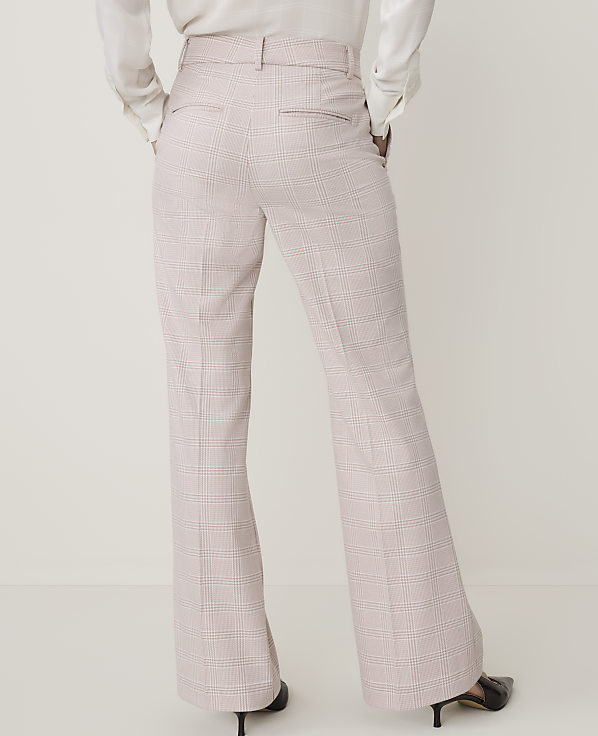 A person wearing light pink plaid flared trousers and a white blouse stands against a plain white background.