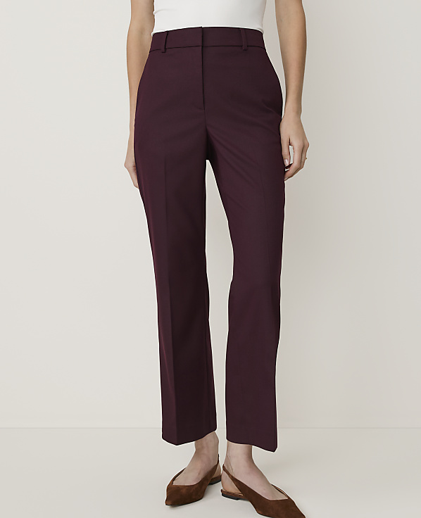 A person stands in the foreground wearing burgundy trousers and flat shoes against a plain white background.