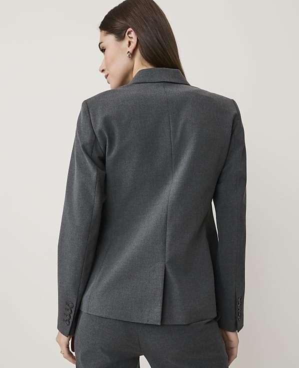 A woman in a grey blazer and pants stands against a plain white background.