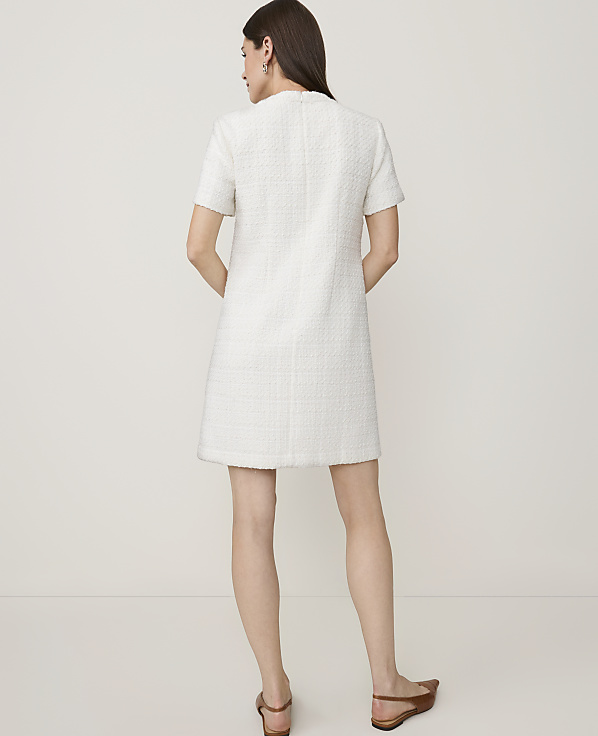 A woman in a white tweed dress stands against a plain white background.