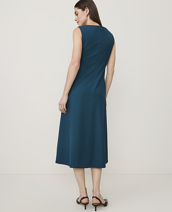 A woman in a teal dress stands against a plain, light-colored background.
