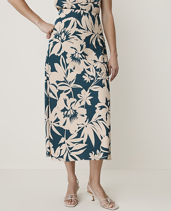 A woman in a floral print skirt and light-colored heels stands against a plain, light background.