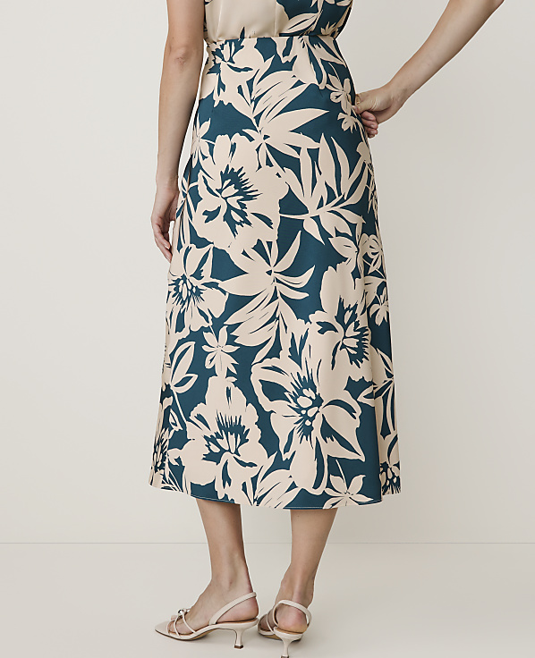 A woman in a floral skirt stands against a plain, light-colored background.
