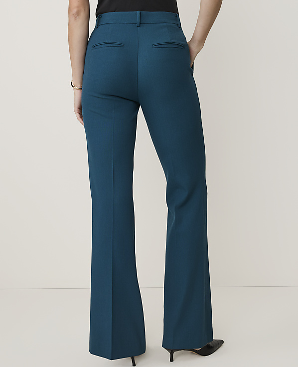 A person wearing teal flared dress pants stands against a plain, light-colored background.