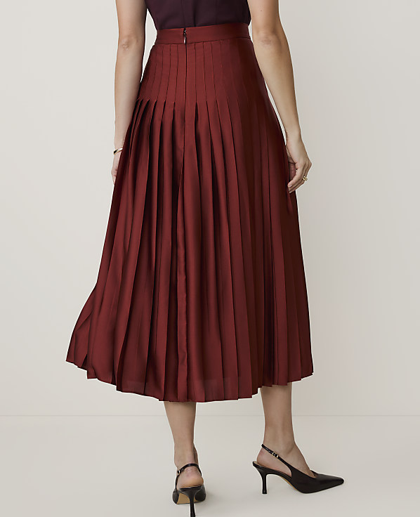 A woman in a maroon pleated skirt and black heels stands against a plain, light-colored background.