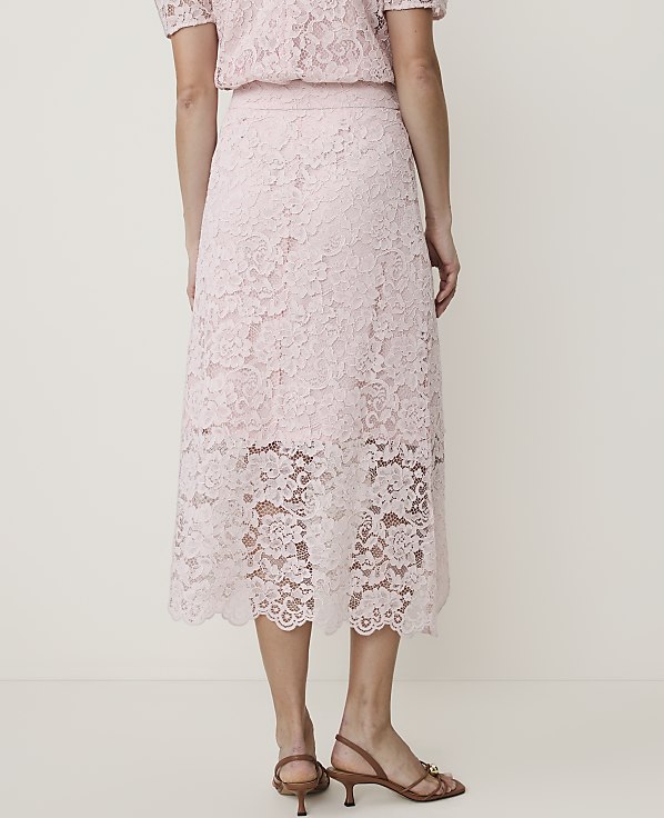 A person stands in a light pink lace skirt and top, with a plain white background.