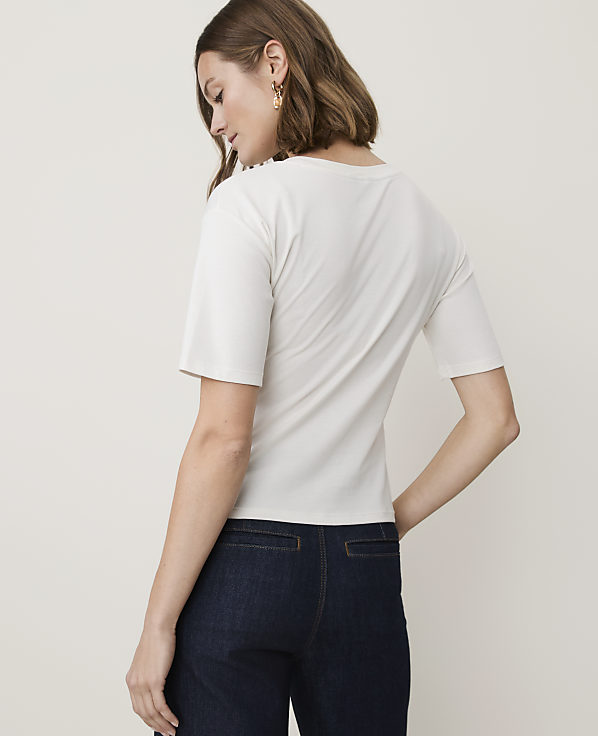 A woman in a white t-shirt and dark jeans stands against a plain white background.