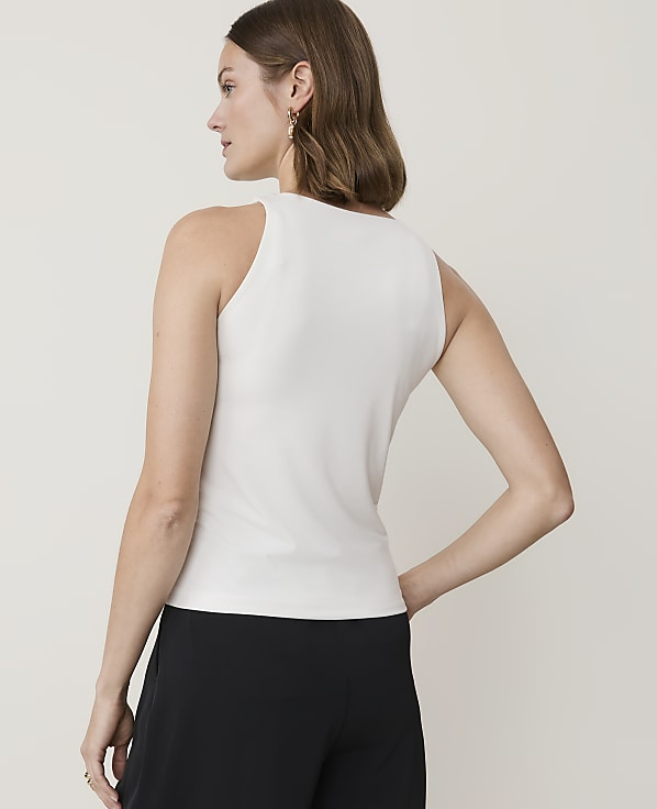 A woman in a white tank top and black pants stands against a plain, light-colored background.