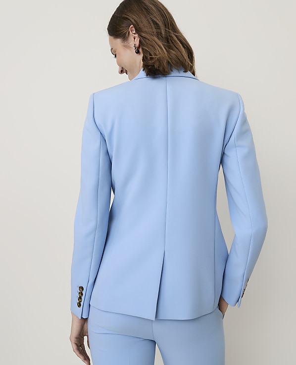 A woman in a light blue blazer and pants stands against a plain, light background.