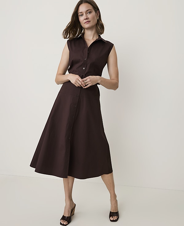 A woman in a brown sleeveless shirt dress stands against a plain white background.