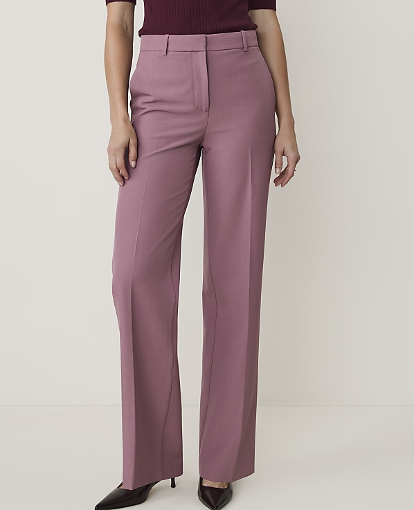 A person in mauve wide-leg trousers and a dark top stands against a plain, light background.
