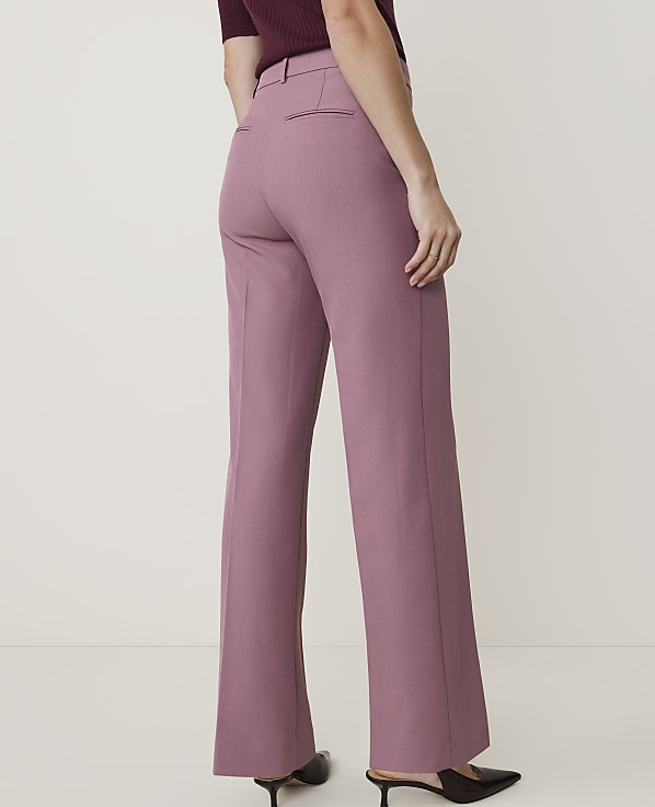 A person wearing rose-colored flared trousers and black pointed-toe heels stands against a plain, light-colored background.