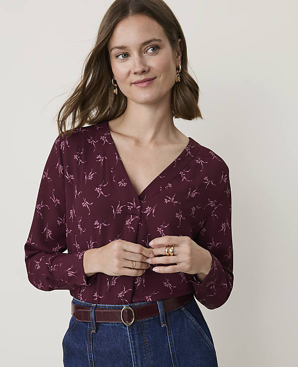 A woman in a burgundy floral blouse and denim jeans stands against a plain, light background.