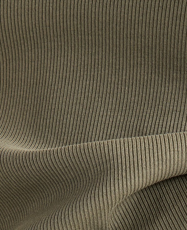 A close-up view of olive green ribbed fabric shows a folded hem in the foreground against a backdrop of vertical ribbing.