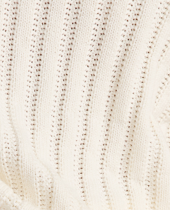 A close-up view of a cream-colored knitted fabric with a textured, ribbed pattern and small, openwork details fills the frame.