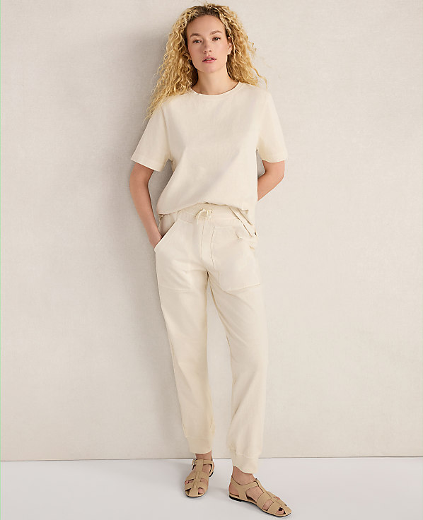 A woman in a cream-colored outfit stands against a textured, light-colored wall.