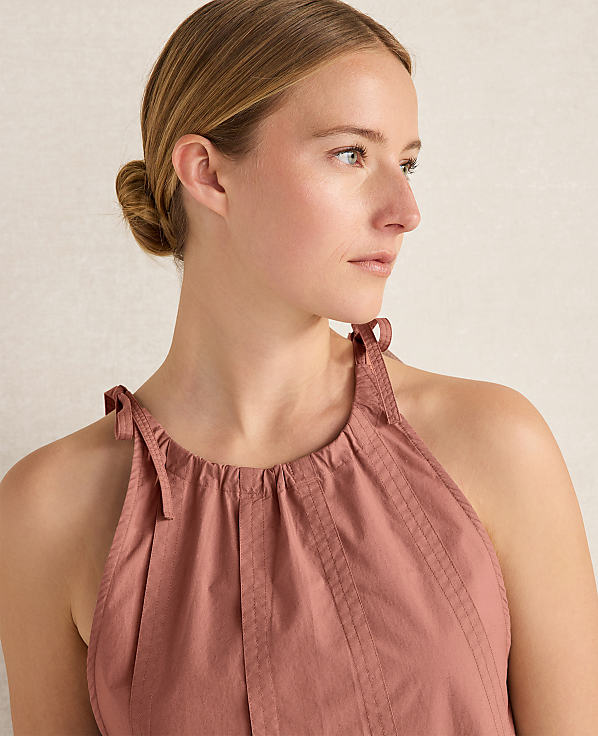A woman with her hair in a bun looks to the right, wearing a pink halter top against a plain, light-colored background.