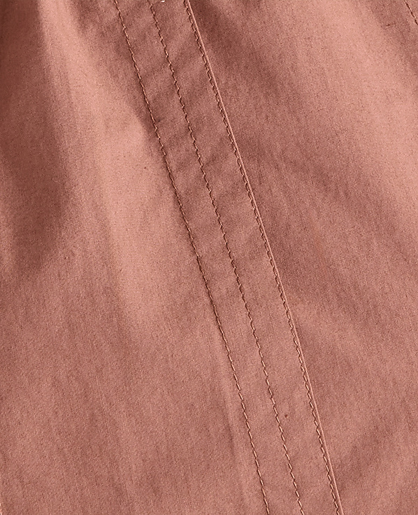 A close-up view of a dusty rose fabric with visible stitching runs diagonally across the frame.