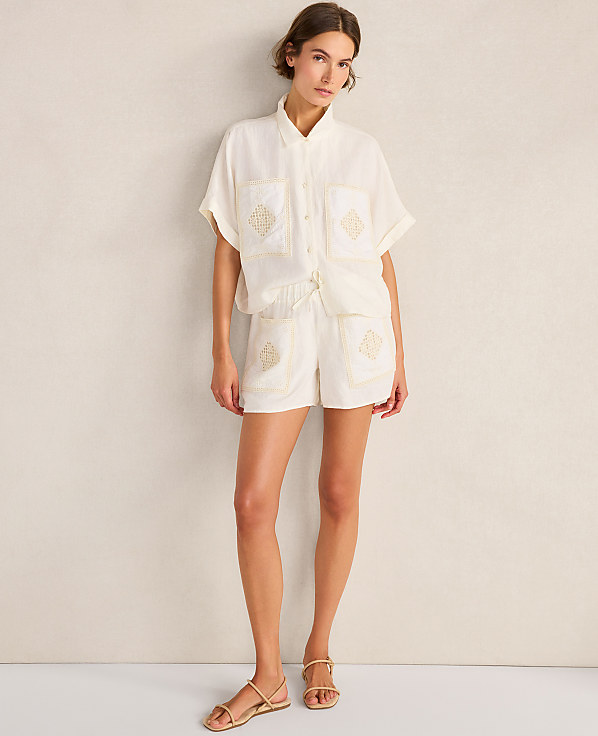 A woman in a cream-colored embroidered shorts set stands against a textured cream wall.