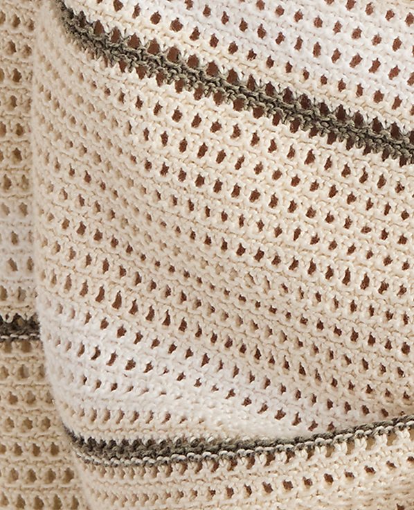 A close-up of a cream-colored crocheted fabric with thin, dark stripes is visible against a blurred, light background.
