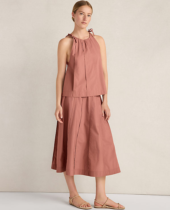 A woman in a rose-colored halter top and skirt stands against a textured, light-colored wall.