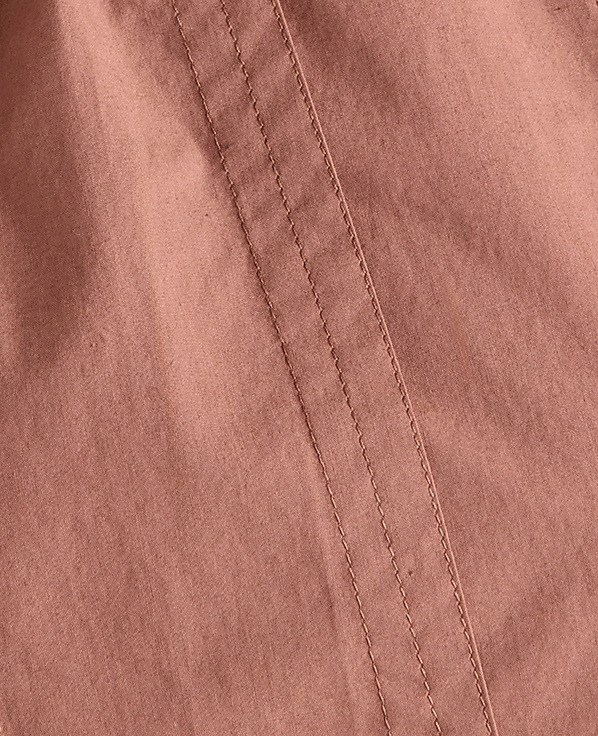 A close-up of a pink fabric with visible stitching runs diagonally across the frame, with soft folds creating subtle shadows in the background.
