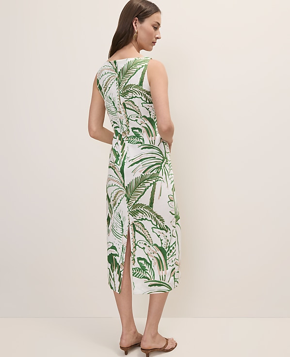 A woman in a white dress with a green tropical leaf print stands against a plain, light-colored background.