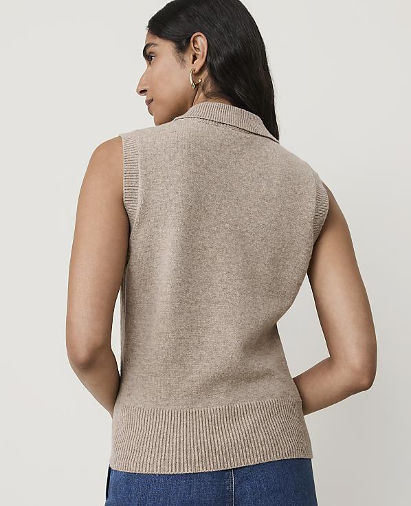 A woman in a beige sleeveless sweater vest stands against a plain white background.
