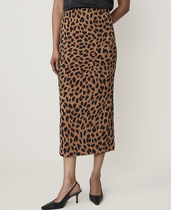 A woman in a leopard print midi skirt and black heels stands against a plain white background.