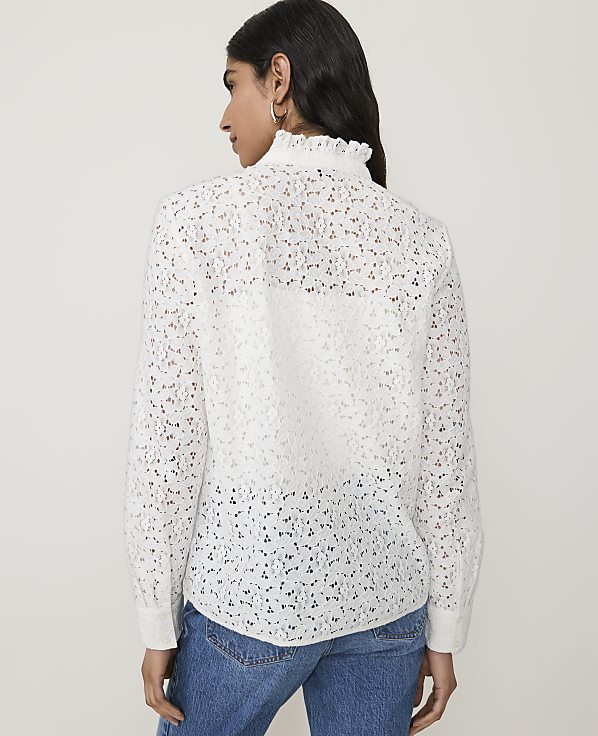 A woman in a white lace blouse and blue jeans stands against a plain white background.